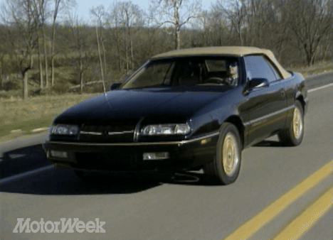 A Black Car With A Tan Top Is Driving Down A Road With Motorweek Written On The Bottom GIF