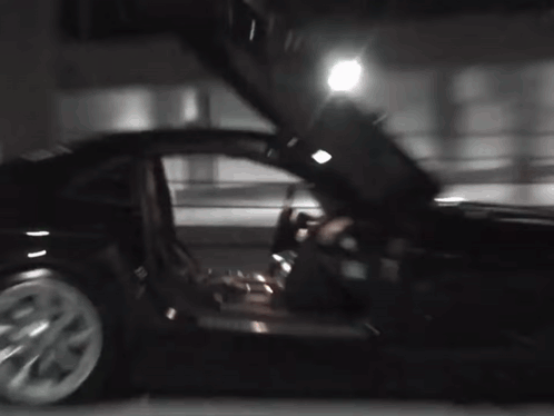 A Black Car With Its Doors Open Is Parked In A Parking Lot At Night . GIF