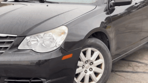 A Black Car With Silver Rims And A Black Hood Is Parked On The Side Of The Road GIF