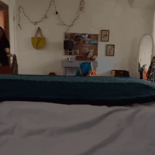 A Black Cat Is Standing On A Bed In A Room GIF