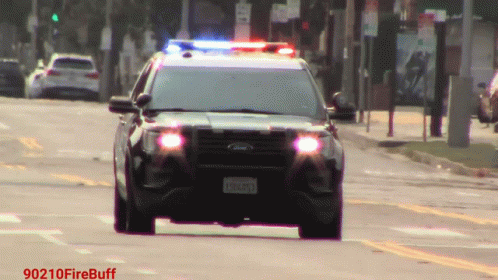 A Black Ford Police Car Is Driving Down A Street With A License Plate That Says Eh6093 GIF