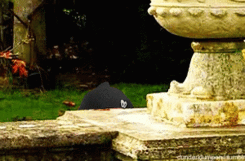 A Black Hat With A Heart On It Is Sitting On A Stone Ledge Next To A Statue .. GIF