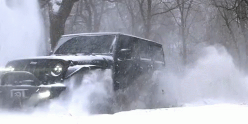 A Black Jeep Is Driving Through A Snowy Forest . GIF