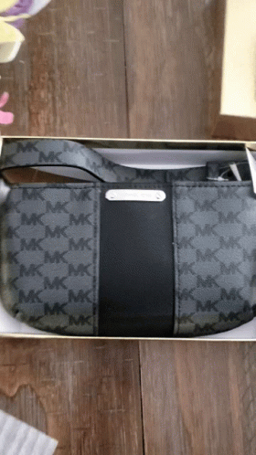A Black Michael Kors Purse Is In A Box On A Wooden Table GIF