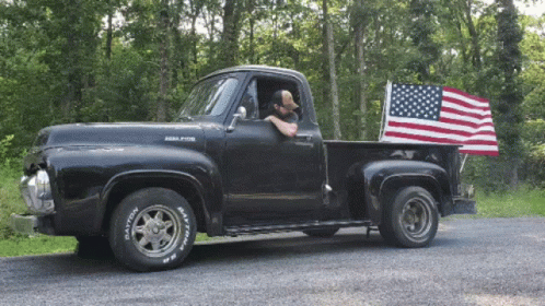 A Black Pickup Truck With Dayton Tires And An American Flag On The Back GIF