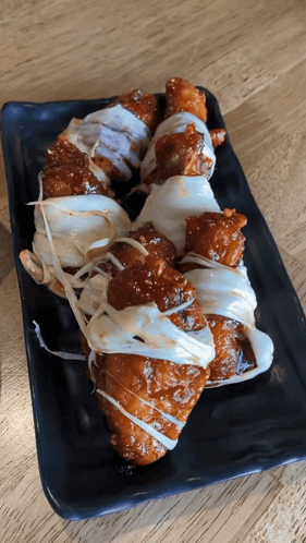 A Black Plate Topped With Fried Chicken Covered In Sauce And Cheese GIF