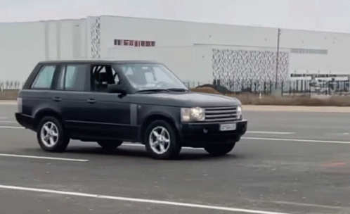 A Black Range Rover Is Driving Down A Road In Front Of A Large White Building GIF