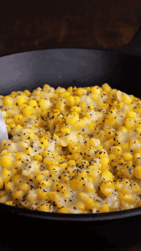 A Black Skillet Filled With Corn And Cheese With A Spoon In It GIF