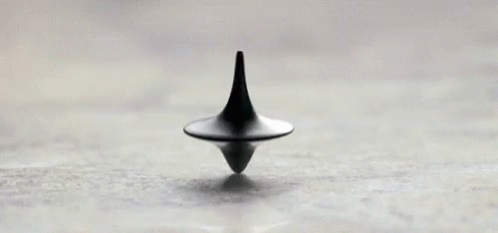 A Black Spinning Top Is Sitting On Top Of A White Surface . GIF