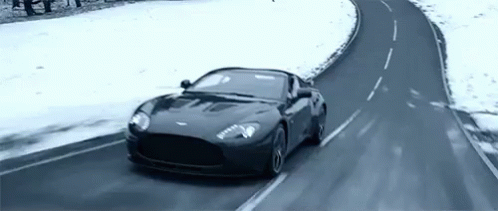A Black Sports Car Is Driving On A Snowy Road . GIF