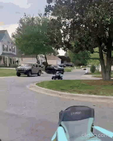a black suv is driving down a residential street next to a lawn mower