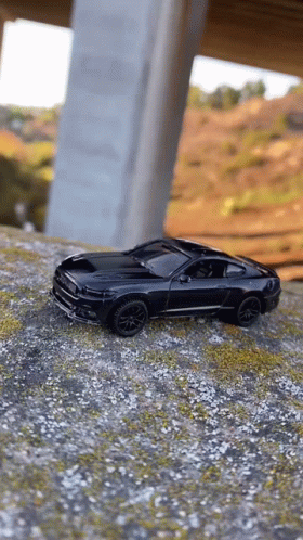 a black toy car is sitting on top of a dirt hill under a bridge .