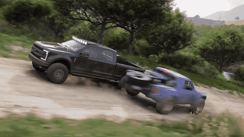 A Black Truck Pulls A Blue Truck On A Dirt Road GIF