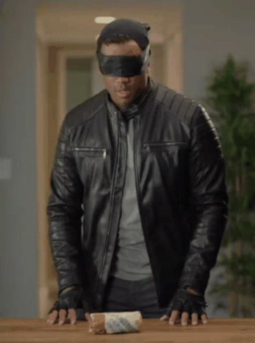 A Blindfolded Man In A Black Leather Jacket Holds A Roll Of Bread GIF