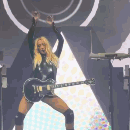 A Blonde Woman In A Black Bodysuit Is Holding A Gibson Guitar GIF