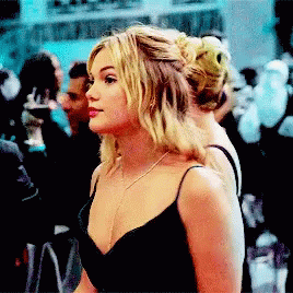 A Blonde Woman In A Black Dress Is Standing In A Crowd GIF
