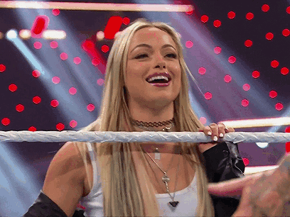 A Blonde Woman Is Standing In A Wrestling Ring Smiling . GIF