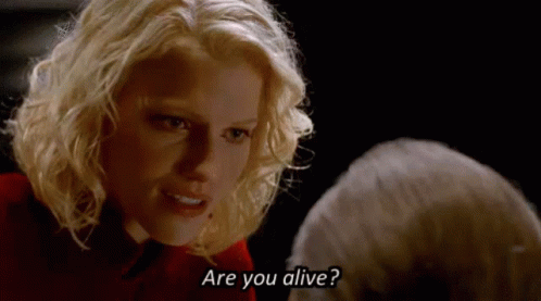 A Blonde Woman Is Talking To A Man In A Dark Room And Asking If He Is Alive . GIF
