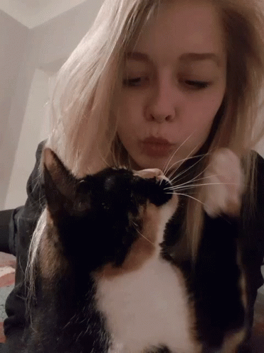 A Blonde Woman Kisses A Black And White Cat On The Nose GIF