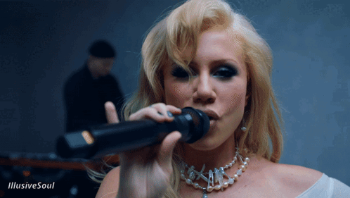 A Blonde Woman Singing Into A Microphone With The Words Illusive Soul Behind Her GIF