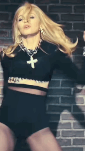 A Blonde Woman Wearing A Black Crop Top And Shorts With A Cross Necklace GIF