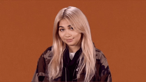 A Blonde Woman Wearing A Camouflage Jacket Looks At The Camera GIF