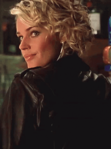 A Blonde Woman Wearing A Leather Jacket And A Blue Top Smiles GIF