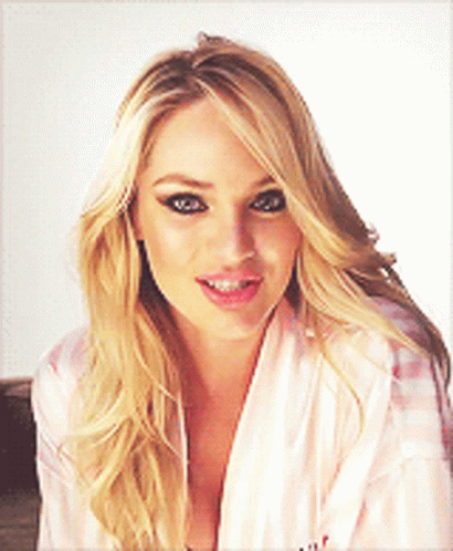 A Blonde Woman Wearing A Pink Robe Is Smiling And Looking At The Camera GIF