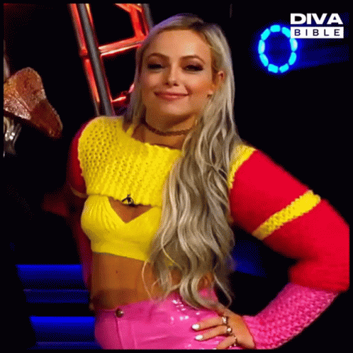 A Blonde Woman Wearing A Yellow And Pink Sweater And Pink Pants Is Standing In Front Of A Diva Bible Sign GIF