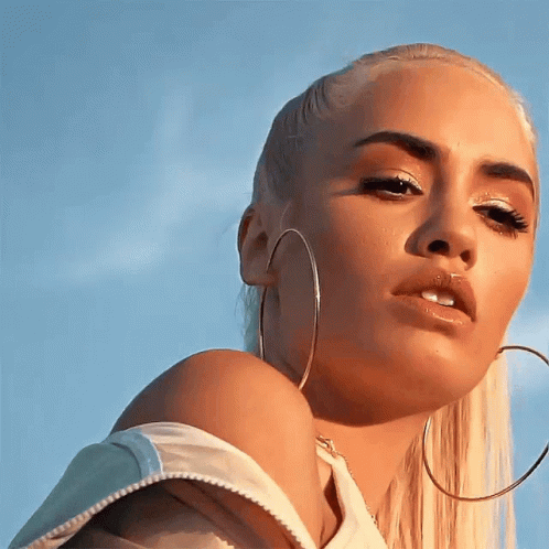 A Blonde Woman Wearing Hoop Earrings Looks At The Camera GIF