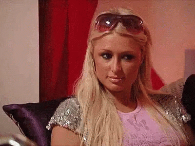 A Blonde Woman Wearing Sunglasses Is Sitting On A Couch . GIF