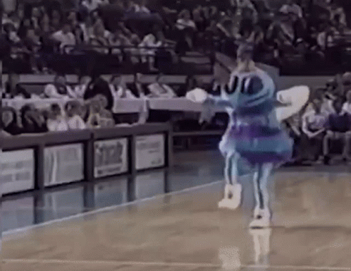A Blue And Purple Mascot Is Dancing On A Basketball Court In Front Of A Crowd . GIF