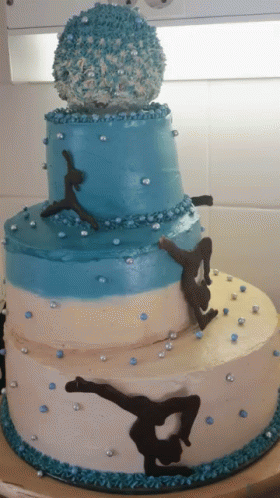 A Blue And White Cake With A Gymnast On Top GIF