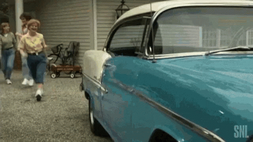A Blue And White Car Is Parked In A Driveway Next To A Group Of People . GIF