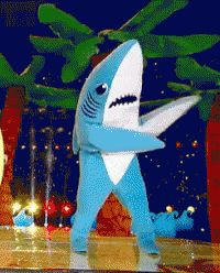 A Blue And White Shark Costume Is Standing On A Stage GIF