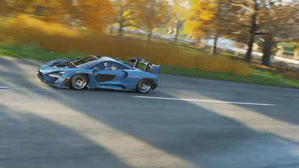 A Blue And White Sports Car Is Driving Down A Road GIF