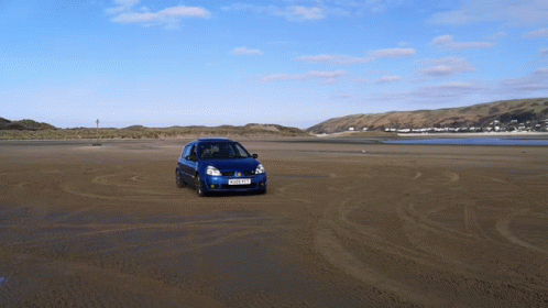 A Blue Car Driving On A Sandy Beach With A License Plate That Says Ykp Xkf GIF