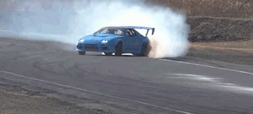 A Blue Car Is Drifting On A Road And Smoke Is Coming Out Of The Tires GIF