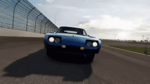 a blue car is driving down a race track with a fence in the background