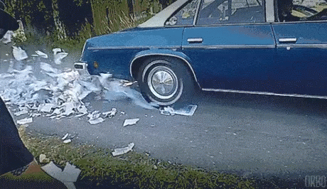 A Blue Car Is Driving Down A Road With A Flat Tire And Smoke Coming Out Of It . GIF