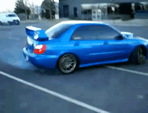 A Blue Car Is Driving Down A Street With Smoke Coming Out Of The Tires GIF