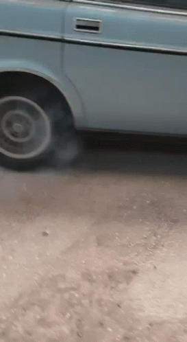 A Blue Car Is Parked On A Dirt Road And Smoke Is Coming Out Of The Tire GIF