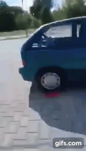 A Blue Car Is Parked On The Side Of The Road With A White Wheel GIF