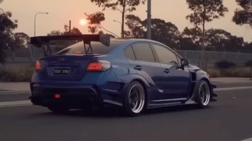 A Blue Car With A Spoiler On The Roof Is Driving Down A Road . GIF