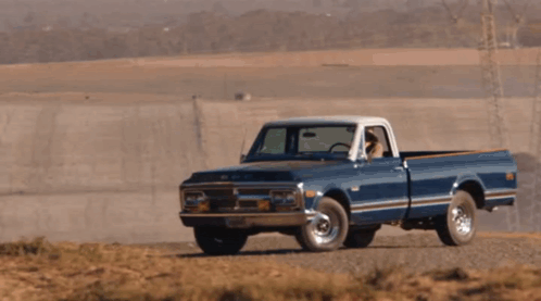 A Blue Chevrolet Truck Is Driving Down A Dirt Road In The Desert GIF