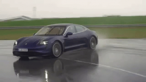 a blue porsche taycan is driving down a wet road .