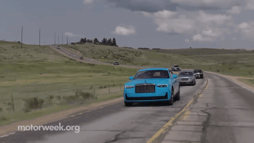 A Blue Rolls Royce Is Driving Down The Road With Other Cars GIF
