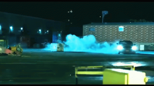 A Blue Smoke Coming Out Of A Car In A Parking Lot At Night GIF