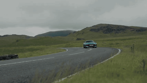 A Blue Sports Car Is Driving Down A Road With Mountains In The Background And A License Plate That Says Ycs Jml GIF