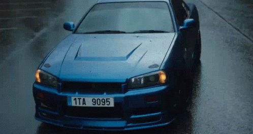 A Blue Sports Car With A License Plate That Says 1Ta 9095 Is Driving Down A Wet Street . GIF